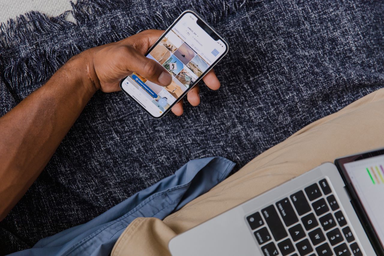 Hand holding smartphone with open laptop, showcasing modern digital lifestyle.